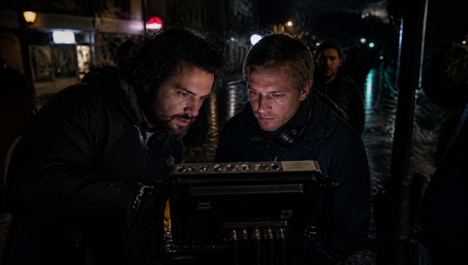 Director and cinematographer studying a monitor on a rain-slick night location