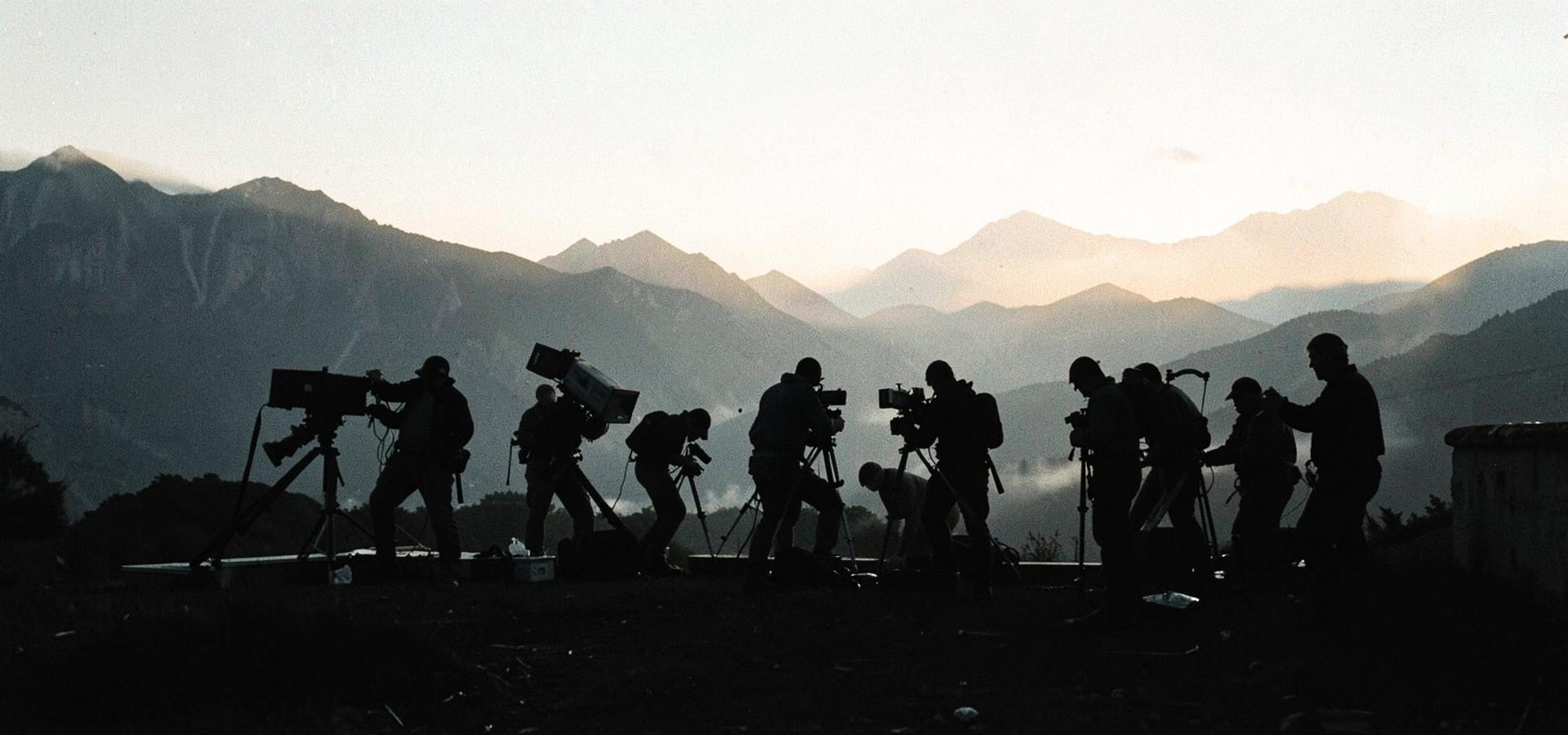 Silhouetted film crew setting up cameras at dawn on a mountain location